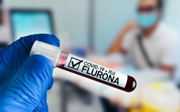 Nurse holding a vial of blood titled COVID-19 + Flu - FLURONA